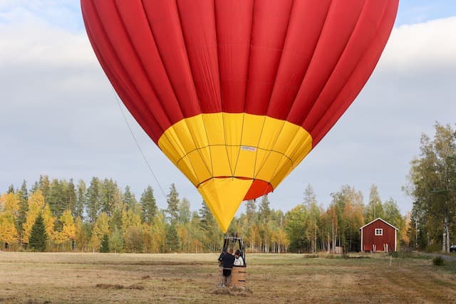 Nederdel av ballong som står upp på slagen åker med höstfärgad skog i bakgrunden